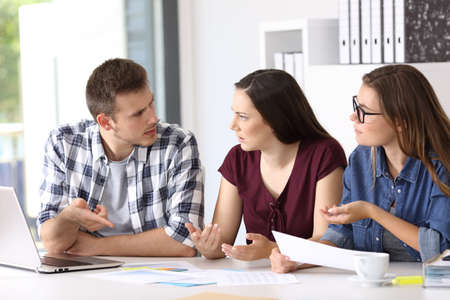Three employees having a job conversation sitting in a desktop at officeの写真素材