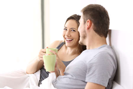 Happy couple having breakfast and talking on a bed of an hotel room or homeの写真素材