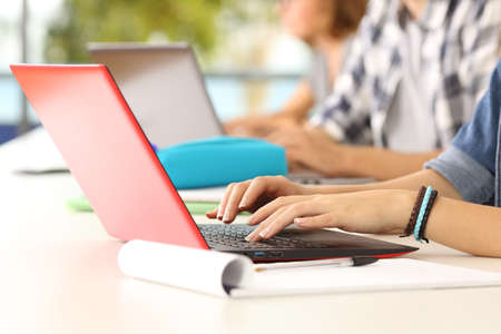 Side view close up of three student hands learning on line typing in their laptops in a classroomの写真素材