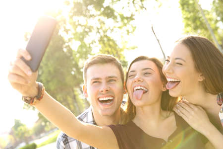 Back light of three funny teens taking selfies and joking in the streetの写真素材