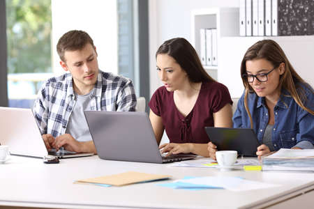 Three attentive employees working on line together with multiple devices at office