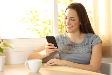 Single girl chatting on a mobile phone sitting in a table at homeの写真素材