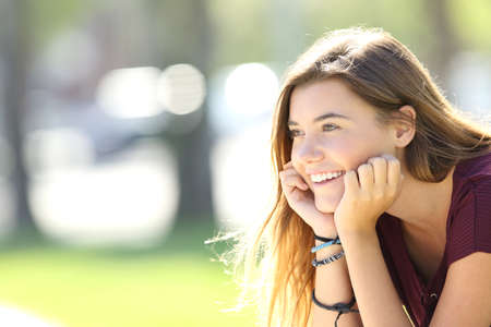 Portrait of a single happy teen smiling and looking away sitting in a parkの写真素材