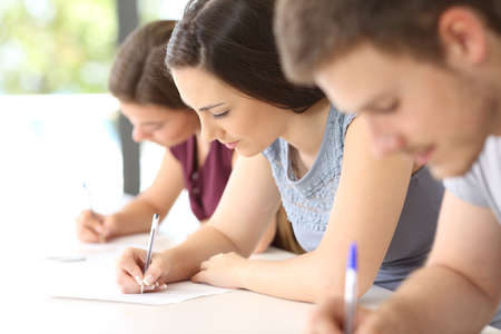 Close up of three concentrated students doing an exam in a classroomの写真素材