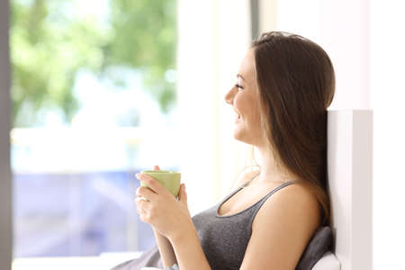 Side view of a happy single woman having breakfast on the bed of an hotel room or apartmentの写真素材