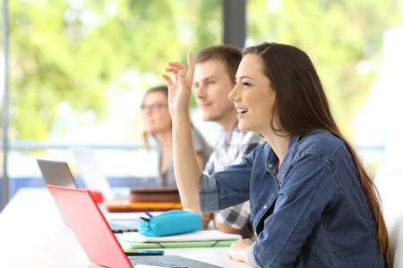 Side view of a student raising arm sitting in a classroom with classmates in the background