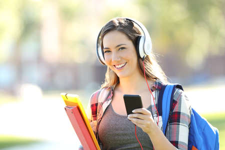 Beautiful student wearing headphones listening music and looking at you in the streetの写真素材