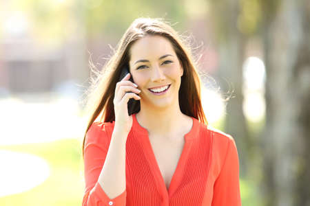 Front view portrait of a happy woman wearing an orange blouse calling on phone and looking at you in the streetの写真素材