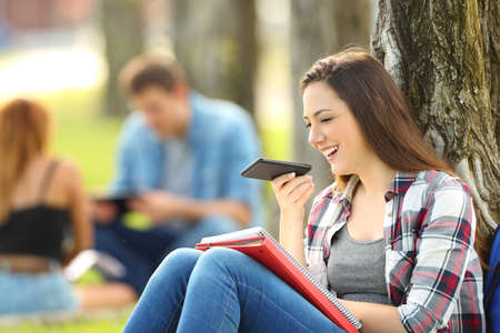 Student using voice recognition with a smart phone to record notes sitting on the grass in a parkの写真素材