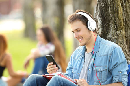 Student learning listening audio tutorials in a park sitting on the grass in a parkの写真素材
