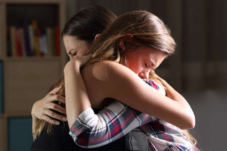 Side view of two sad good friends embracing in a bedroom in a house interior with a dark light in the backgroundの写真素材