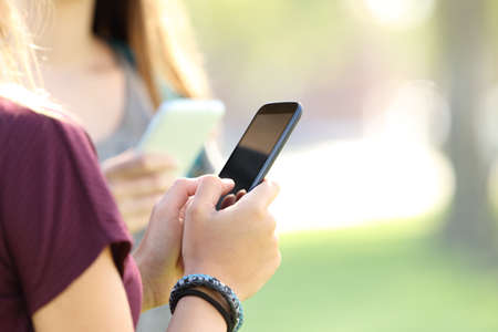 Hands of two teen girls using smart phones in the streetの写真素材