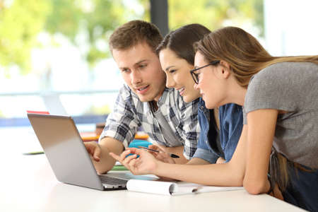 Three students learning together on line with a laptop in a classroomの写真素材