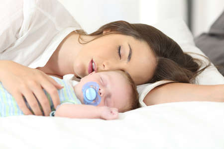 Tired mother sleeping with her baby on a bed at homeの写真素材