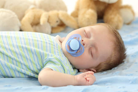 Cute baby sleeping with a pacifier on a bed