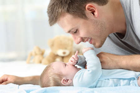 Side view portrait of a baby and father playing together on a bed
