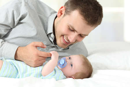Proud father playing with his baby son on a bed at homeの写真素材