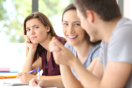 Couple in love and a jealous classmate watching them in a classroom