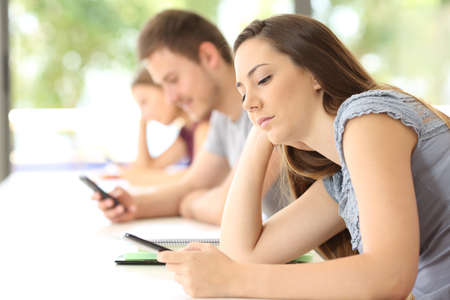 Side view of three bad students distracted using smart phones during a class in a classroomの写真素材
