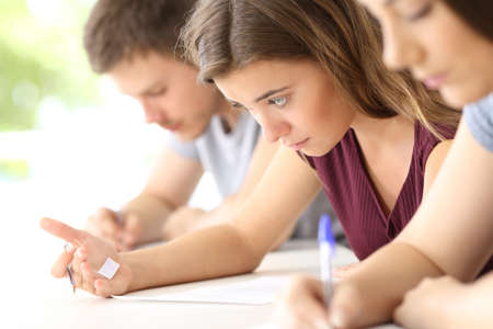 Bad student reading a cheating sheet during an exam in a classroomの写真素材
