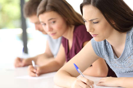 Student trying to copy an exam from another classmate at classroomの写真素材