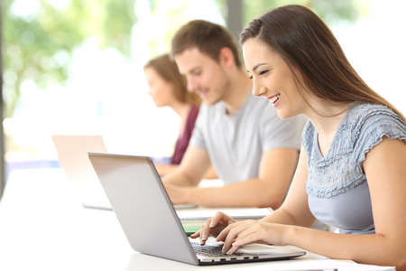 Side view of a happy student searching on line with a laptop at classroomの写真素材