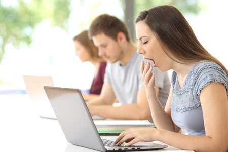 Side view of a tired student yawning using a laptop at classroomの写真素材
