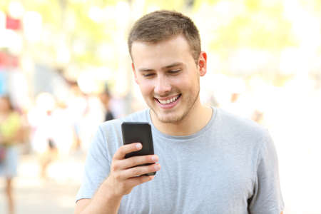 Happy guy using a smart phone and walking on the streetの写真素材