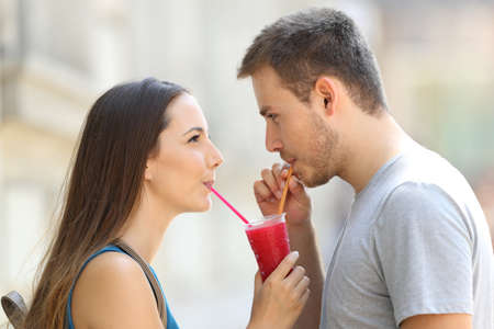 Side view portrait of a happy couple sipping a slush together outdoors in the streetの写真素材