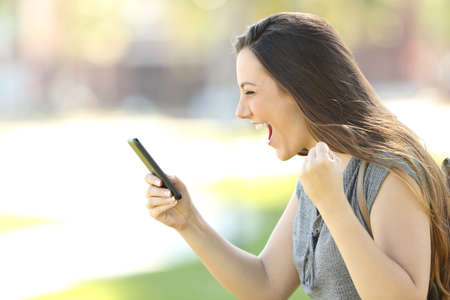 Profile of a single excited woman using a smart phone outdoors in the street