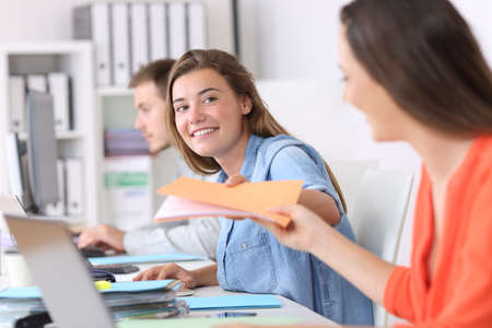 Happy employee giving a documents folder to a colleague at officeの写真素材
