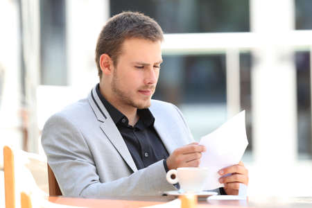 Serious executive reading a letter sitting in a coffee shopの写真素材