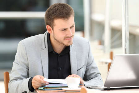 Executive comparing documents on line with a laptop sitting in a coffee shopの写真素材