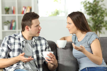 Angry couple arguing sitting on a couch at homeの写真素材