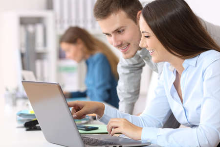 Two happy colleagues coworking on line together with a laptop at office