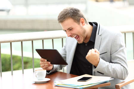 Excited executive receiving good news on line sitting in a coffee shop