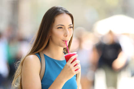 Single girl walking and sipping a slush in the street in summerの写真素材