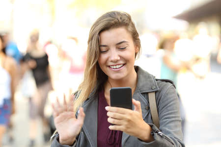 Front view portrait of a happy teen greeting during a videocall on the streetの写真素材