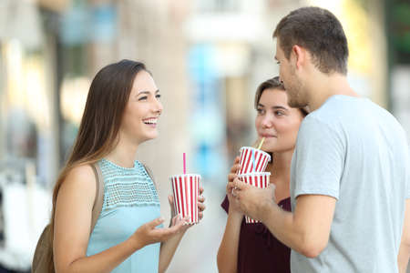 Three happy friends talking and drinking takeaway refreshments standing in the streetの写真素材