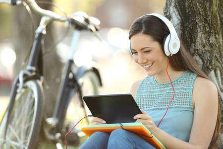 Happy student watching media content on line in a tablet sitting in a parkの写真素材