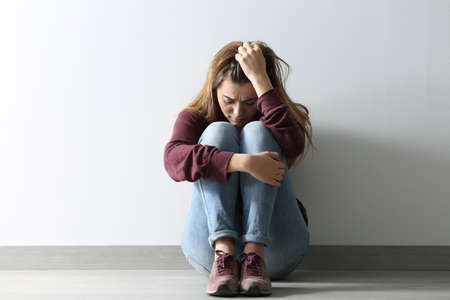 Front view full body portrait of a sad woman sitting on the floor at home