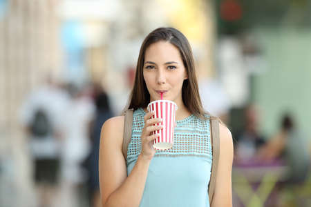 Front view of a girl sipping a takeaway drink walking on the street