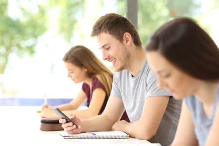 Side view of a student distracted with a mobile phone during a class at classroomの写真素材