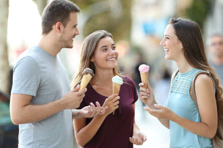 Three happy friends talking and eating ice creams in the streetの写真素材