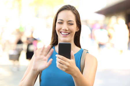 Happy lady greeting during a video call with a smart phone on the streetの写真素材
