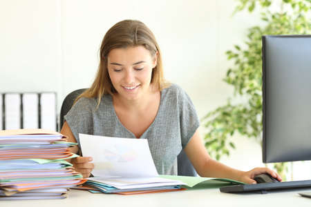 Front view of a happy employee reading reports sitting in a desktop at officeの写真素材