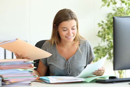 Happy employee managing documents sitting in a desk at office