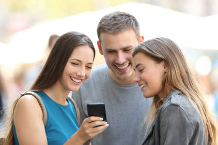 Three happy friends sharing smart phone content on the streetの写真素材