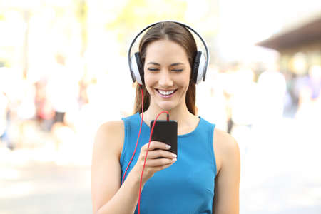 Front view portrait of a girl listening to music on a phone wearing headphones on the streetの写真素材