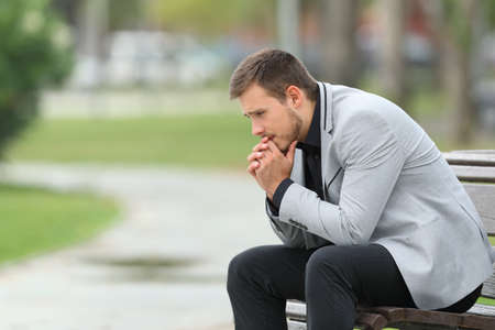 Side view portrait of a worried businessman sitting on a bench in a parkの写真素材